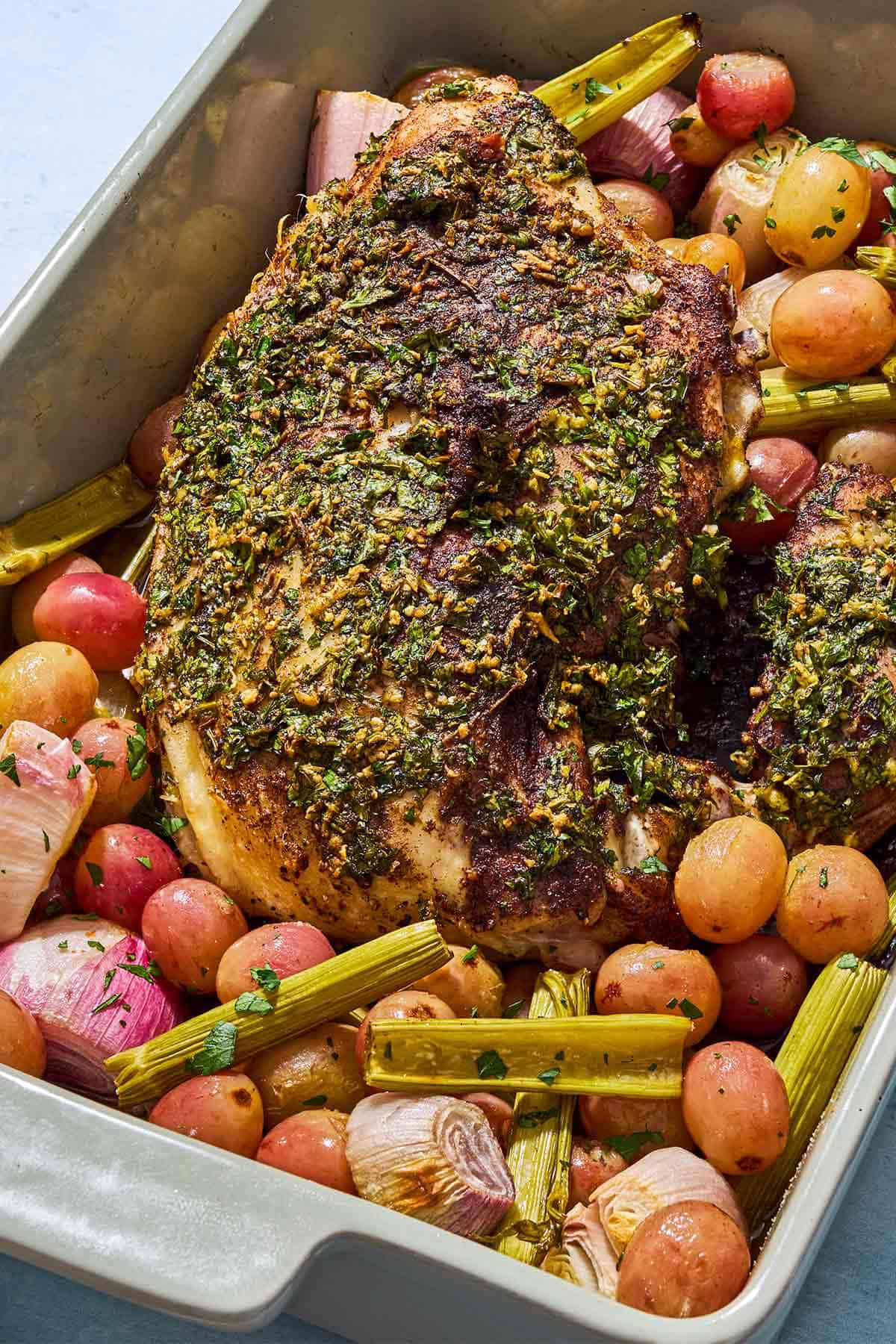 A close up of roast turkey breast with grapes and vegetables in a baking dish.