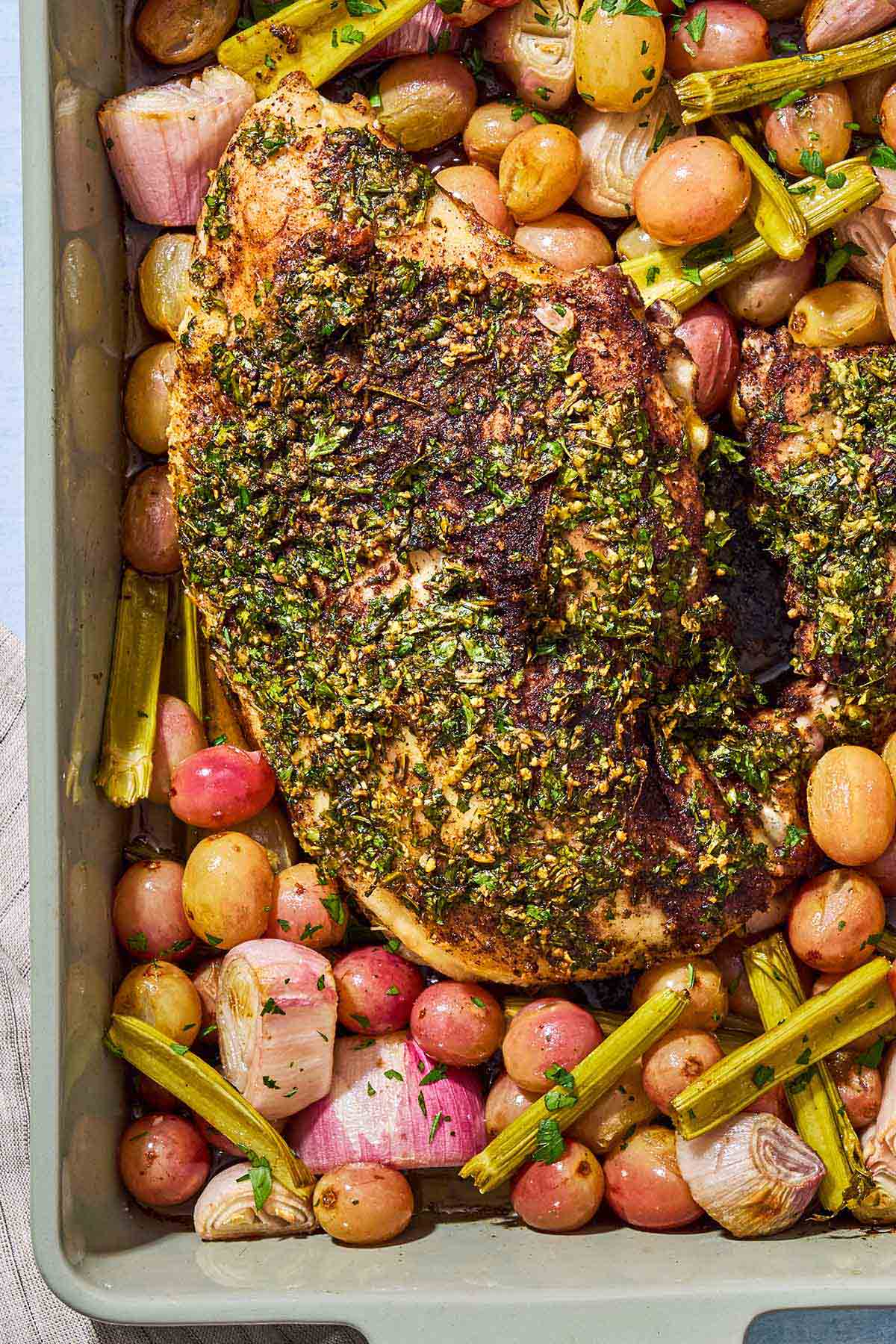 An overhead photo of roast turkey breast with grapes and vegetables in a baking dish.