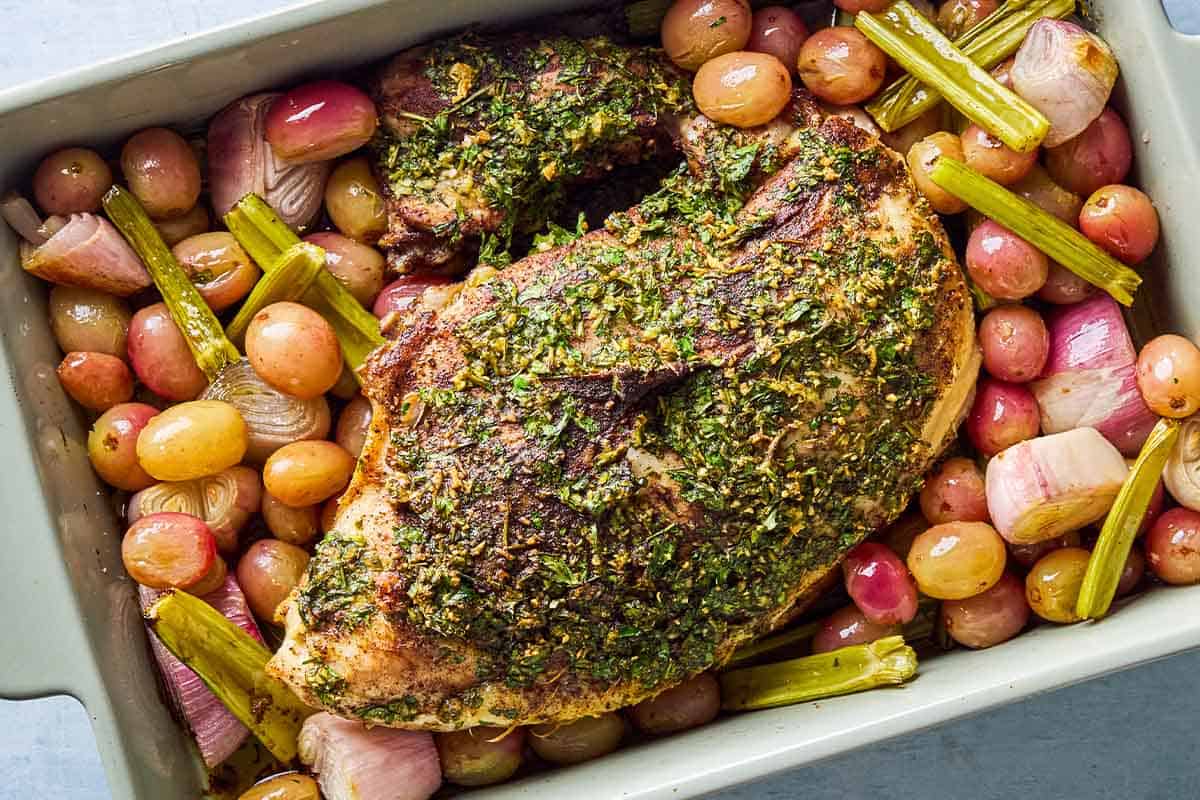 An overhead photo of roast turkey breast with grapes and vegetables in a baking dish.