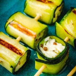 close up of two grilled zucchini roll up skewers on a plate.