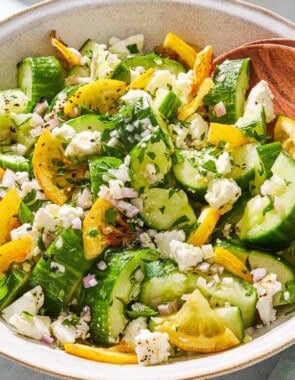 Smashed cucumber salad in a serving bowl with wooden serving utensils.