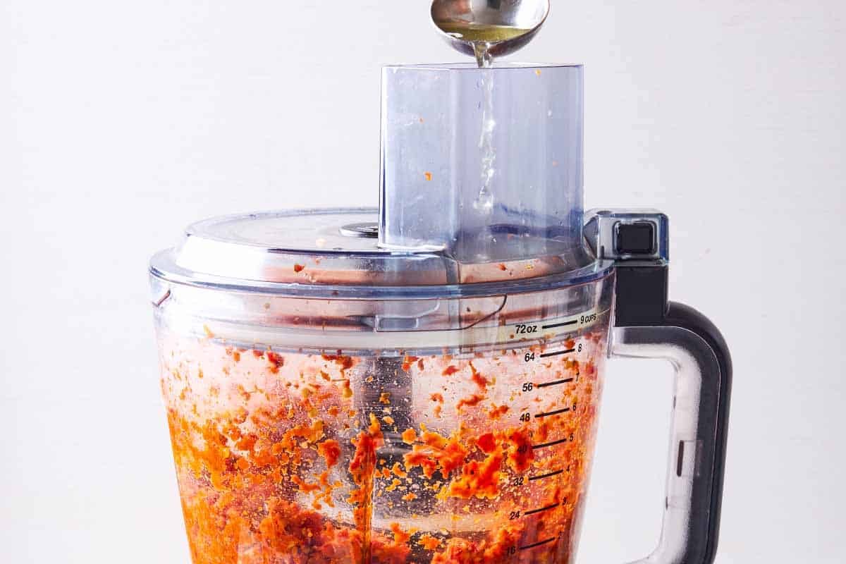 The sun dried tomato's soaking liquid being drizzled onto the sun dried tomato pesto in the bowl of the food processor.