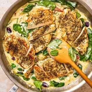 Sun Dried tomato chicken in a skillet with a wooden spoon.