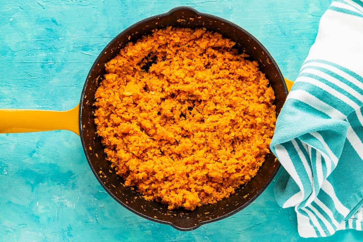 the shredded carrots in a skillet next to a blue and white dish towel.