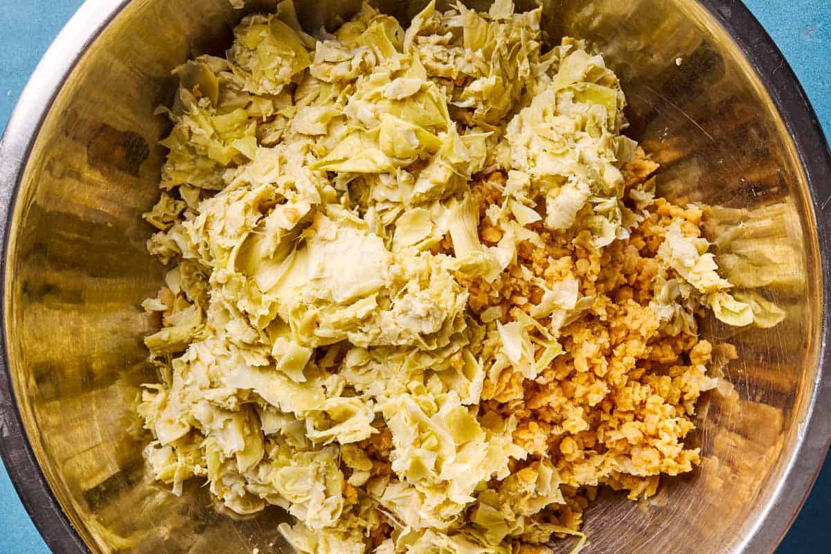 An overhead photo of the processed chickpeas and artichoke hearts for the vegetarian crab cakes in a mixing bowl.