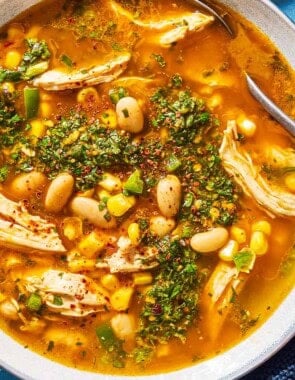 An overhead photo of white chicken chili topped with chermoula in a bowl with a spoon. Next to this is a kitchen towel.