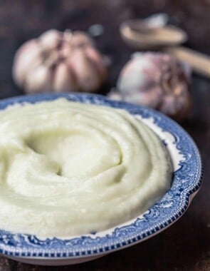 toum garlic sauce in a bowl. two heads of garlic and a spoon to the side