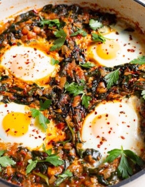 four poached eggs in a saucepan with wilted spinach and fresh parsley.