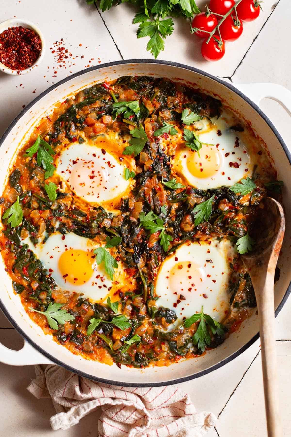 Overhead shot of a pan with Turkish spinach and eggs, showing the 4 poached eggs and saucy wilted spinach mixture.