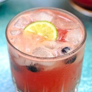 one glass of watermelon sangria, with ice, lime, and blueberries.