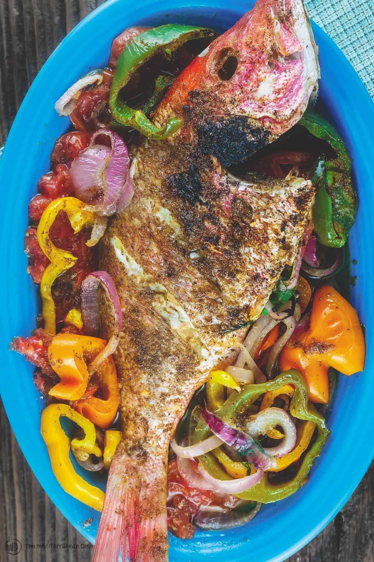 Roasted whole red snapper placed on a bed of vegetables in a dish