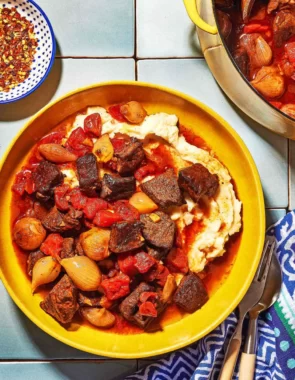 Overhead shot of greek beef stew in a bowl with mashed potatoes and red pepper flakes on the side.